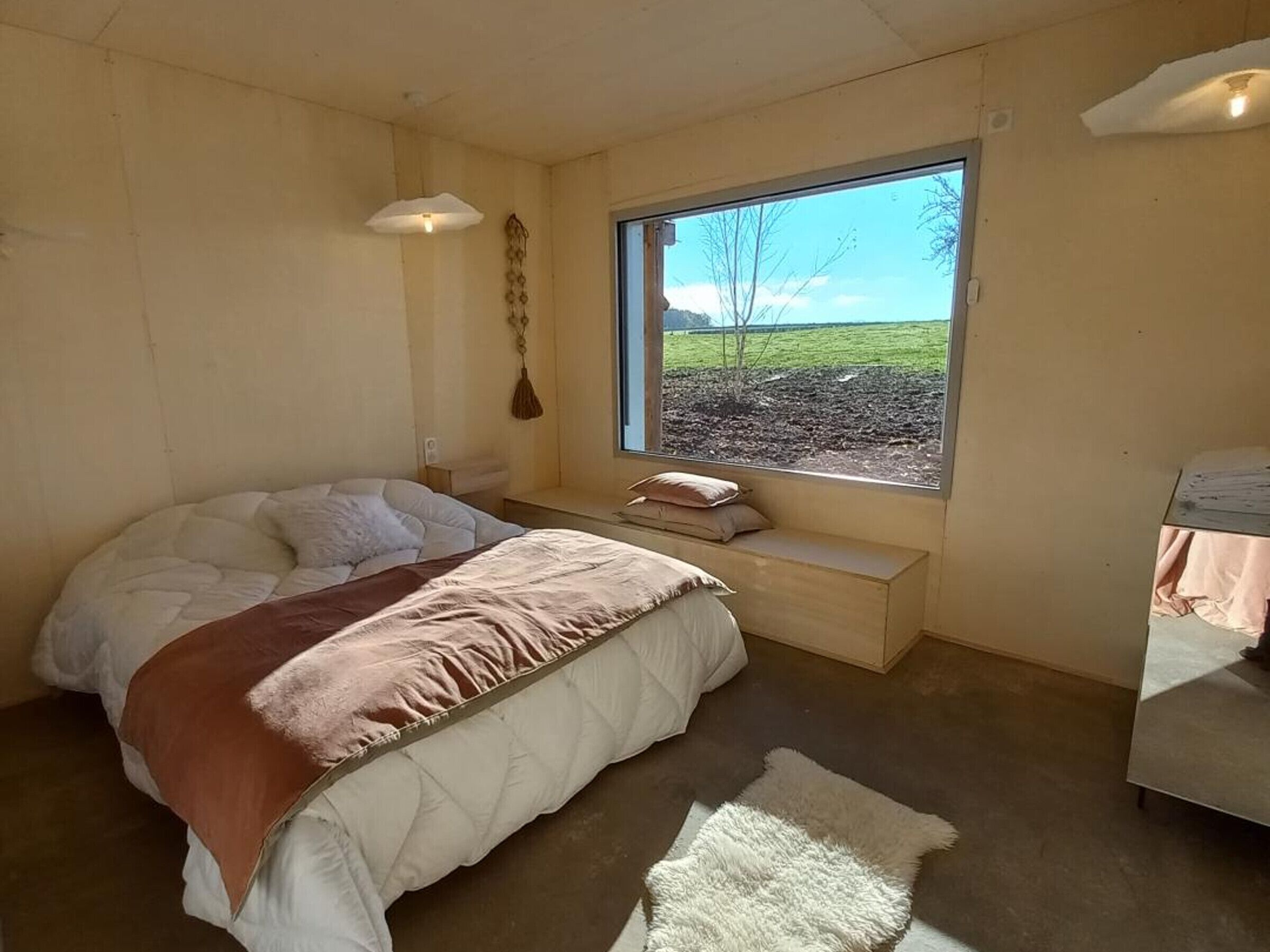 A bedroom with a large bed, a bench, a window with a view of the outdoors, and a small table.