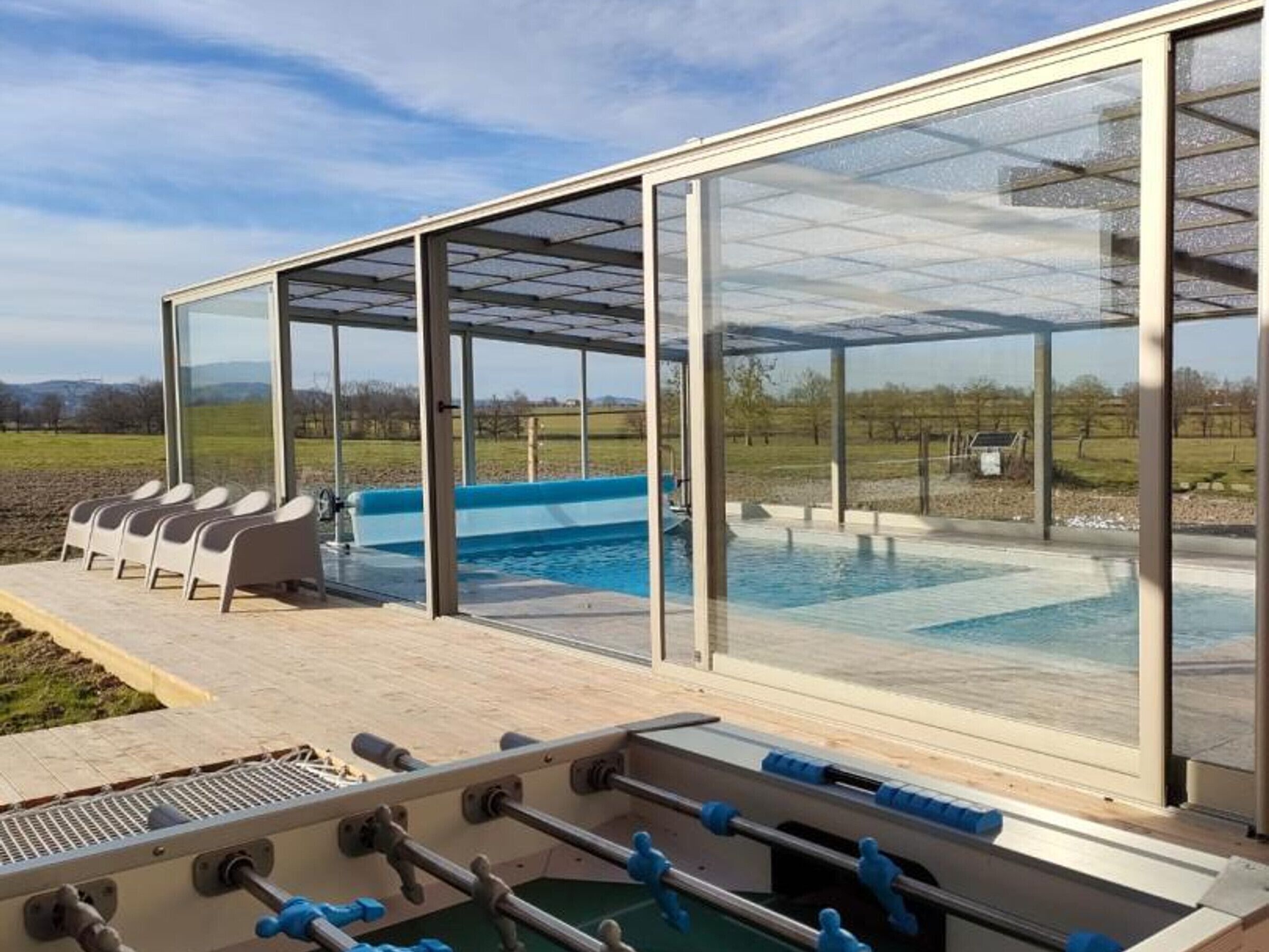 A pool area with a glass-enclosed deck, seating, and a foosball table.