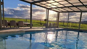 A swimming pool with clear water, surrounded by a covered patio with chairs and a view of a green landscape. - Authentic House with Spa and Pets Allowed (Saint-Forgeux-Lespinasse)