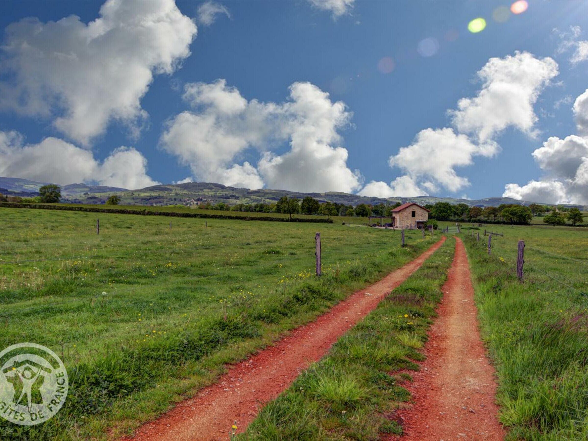 A rural landscape with a dirt path leading to a stone building.