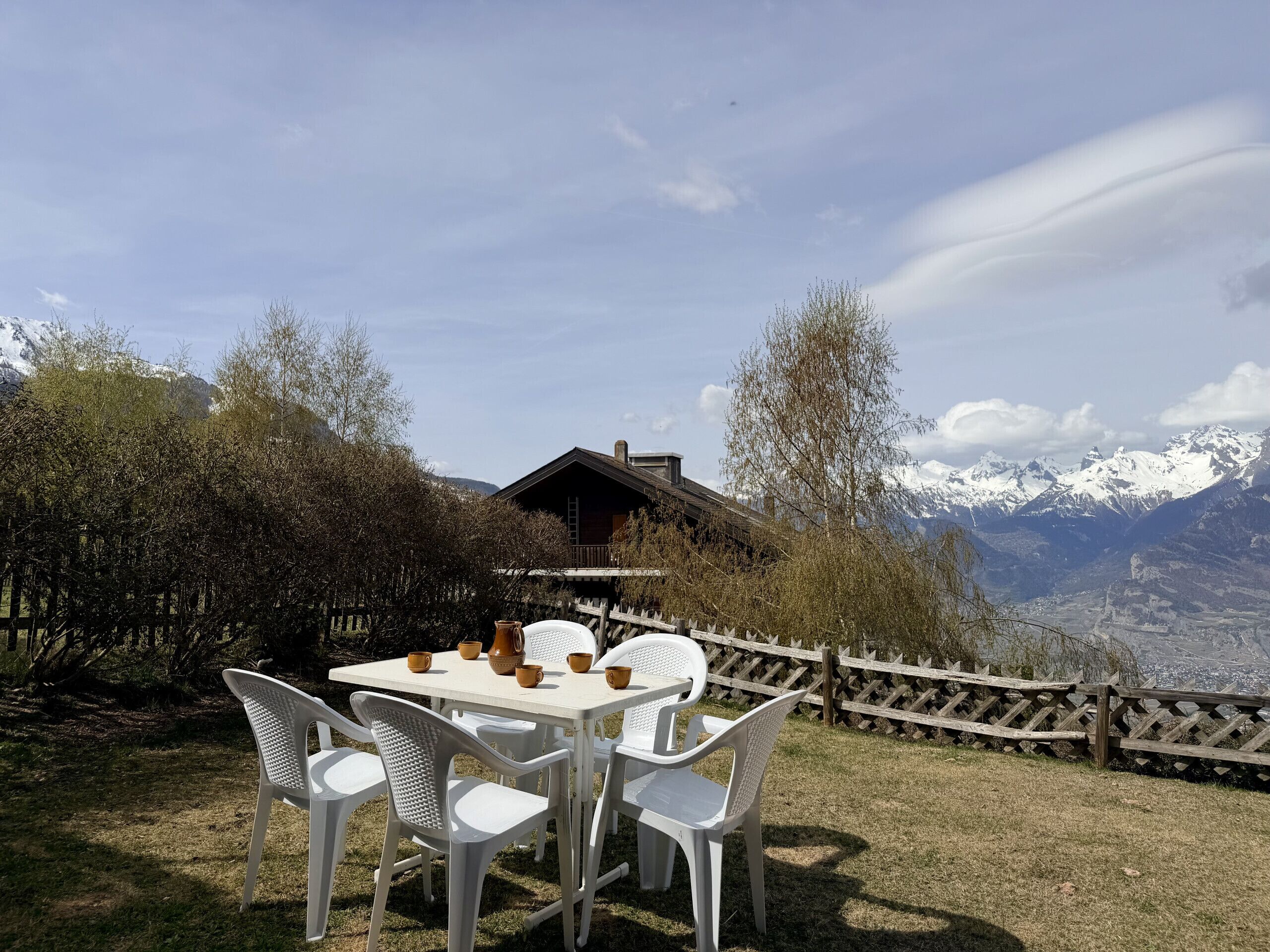 Une table avec des chaises et des tasses, une clôture en bois et une vue sur la montagne.