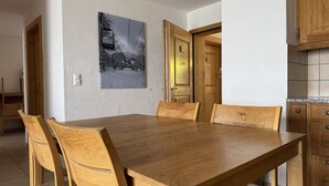 A dining area with a wooden table and chairs, a painting on the wall, and wooden doors.
