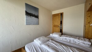 A bedroom with two beds, a wooden wardrobe, and a painting of a snowy landscape.