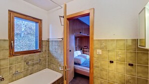 Une salle de bain avec une fenêtre, un lavabo et une porte donnant sur une chambre à coucher équipée d’un lit superposé.