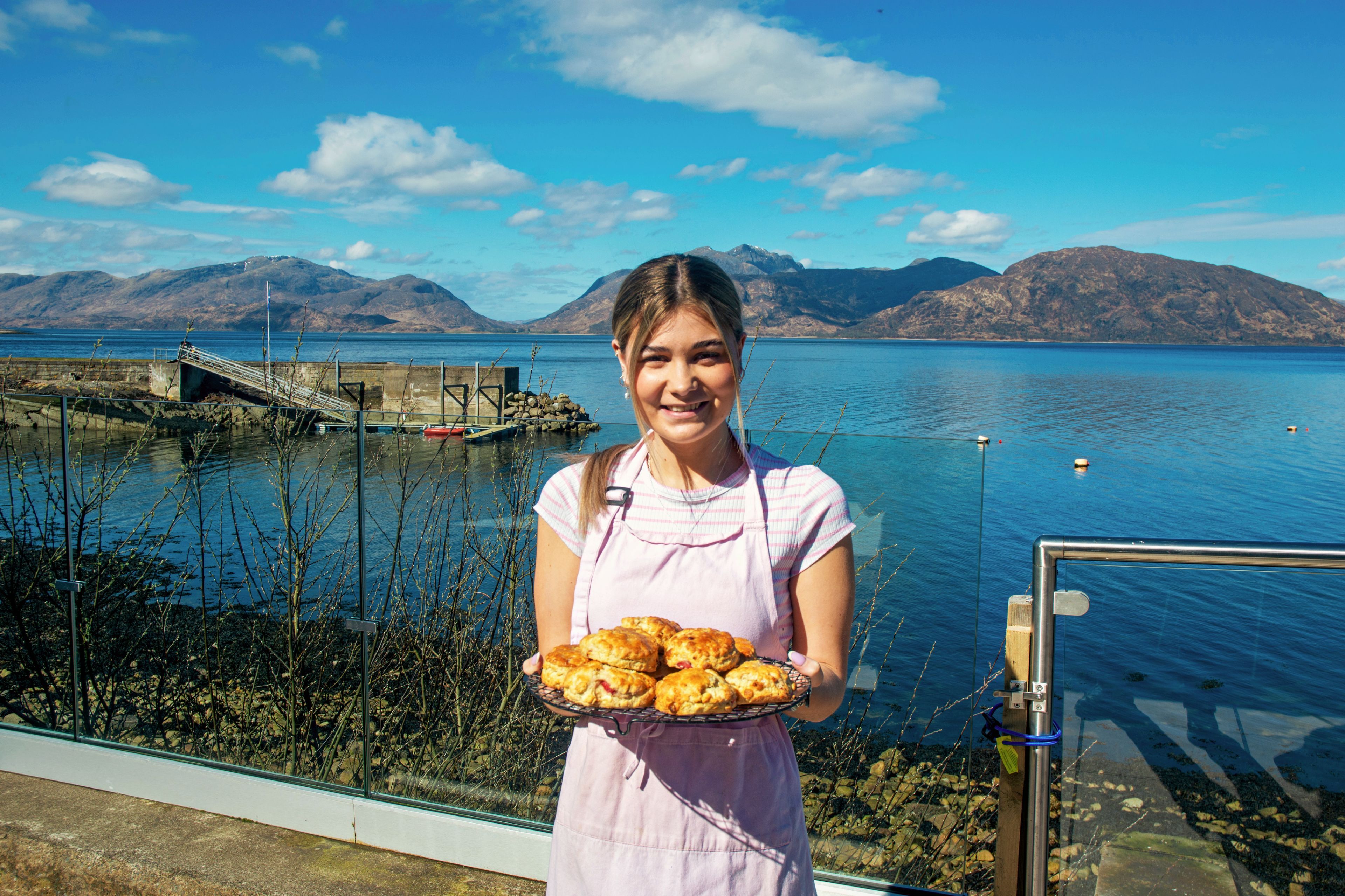 A person holding a tray of food with a scenic view of a lake and mountains in the background.