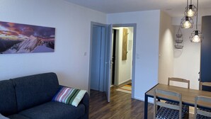 Ein modernes Wohnzimmer mit einem dunkelgrauen Sofa, einem farbenfrohen Streifenpolster, einem Esstisch mit Holzstühlen und einer Deckenleuchte.