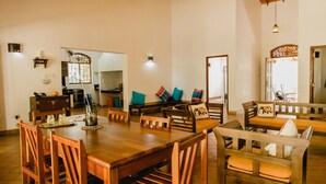 A spacious dining area with a wooden table and chairs, a sofa with colorful cushions, and a ceiling fan. - Lovely Villa near Unawatuna Beach. (Unawatuna)