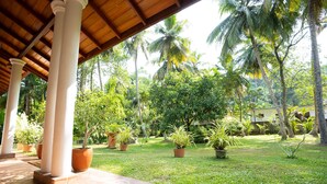 A covered patio area with a tiled floor, surrounded by potted plants and palm trees. - Lovely Villa near Unawatuna Beach. (Unawatuna)