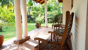 A covered patio with wooden furniture and a garden view. - Lovely Villa near Unawatuna Beach. (Unawatuna)