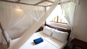 A bed with white linens and a blue towel, a wooden headboard, and a window with a view of greenery. - Lovely Villa near Unawatuna Beach. (Unawatuna)