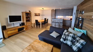 Een moderne woonkamer met een flatscreen televisie, een houten tv-meubel, een donkere bank met decoratieve kussens en een houten salontafel.
