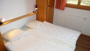 Una cama individual con ropa de cama blanca en una habitación con paredes de madera y una ventana.