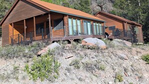 Eine Blockhütte mit Veranda und Balkon, umgeben von felsigem Gelände und Bäumen.