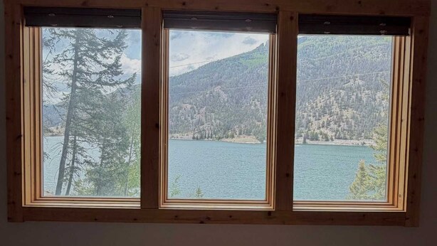 Ein Zimmer mit drei Fenstern und Blick auf einen See und Berge.