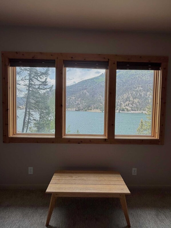 Une pièce dotée de trois fenêtres donnant sur un lac et des montagnes.