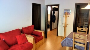 Un espacio habitable pequeño con un sofá de madera, una mesa de comedor con sillas y un perchero de madera.