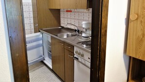 Una cocina compacta con lavamanos, estufa y un refrigerador pequeño.