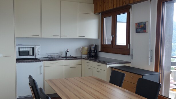 Une cuisine compacte avec des meubles blancs, un four à micro-ondes, une machine à café et un coin repas comprenant une table et des chaises en bois.