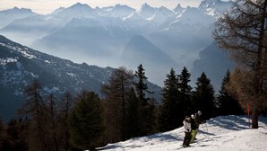 Un paysage montagneux enneigé avec une piste de ski, des arbres et des sommets lointains.