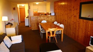 Een ruimtelijke zithoek met een eethoekje, kitchenette en een bank met kussens.