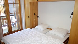 Een slaapkamer met twee eenpersoonsbedden, een houten hoofdbord, een nachtkastje met een lamp en een raam met uitzicht op buitenmeubilair.