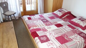 Een slaapkamer met een houten bed, een stoel en een raam met gordijnen.