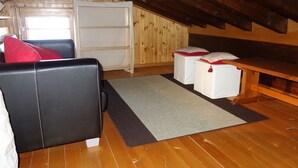 Een knus slaapkamer onder het dak met een houten plafond, een zwarte leren bank, een wit bed met rode kussens en een kleine witte kapstok.