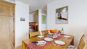 A dining area with a wooden table set for four, a bunk bed in the background, and a painting on the wall. - Plein Ciel VA 032 - MOUNTAIN apartment 6 pers (Veysonnaz)