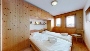 A wooden room with two beds, a chair, and a shelf with decorative items. - Plein Ciel VA 032 - MOUNTAIN apartment 6 pers (Veysonnaz)