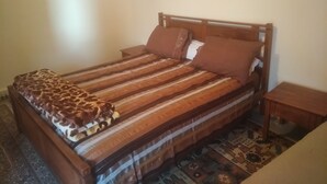 A bed with a striped bedspread and a leopard print blanket, wooden headboard, two bedside tables, and a patterned rug on the floor. - private room with bathroom (Touama)