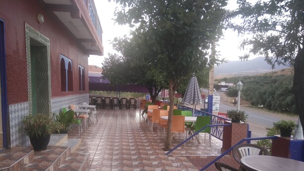 A hotel patio with outdoor seating, a tiled floor, and a view of the road and hills. - private room with bathroom (Touama)