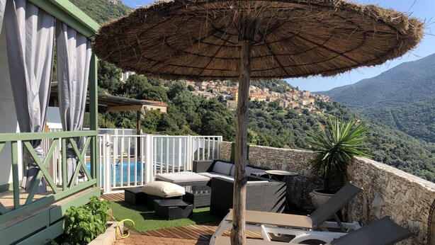 Une terrasse avec piscine, mobilier d’extérieur et vue sur un village perché sur une colline.