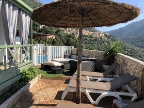 Una terraza con piscina, mobiliario exterior y vistas a un pueblo en la ladera.