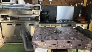 Une cuisine compacte équipée d’un four à micro-ondes, d’une cuisinière et de divers appareils électroménagers. On y trouve une table recouverte d’une nappe à motifs de café et une chaise.