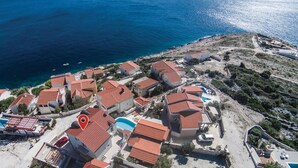Vista aérea de una zona residencial costera con casas de techo rojo, una piscina y una vista despejada del mar.