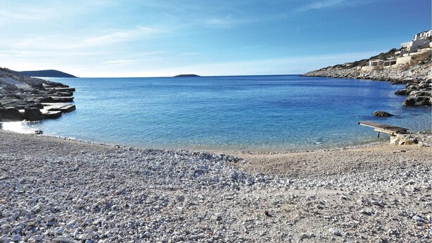 Una playa de guijarros con aguas azules cristalinas y terreno rocoso.