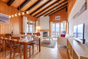 Cozy living area with a high ceiling, wooden dining table, and comfortable sofa, offering a view of the outdoors.