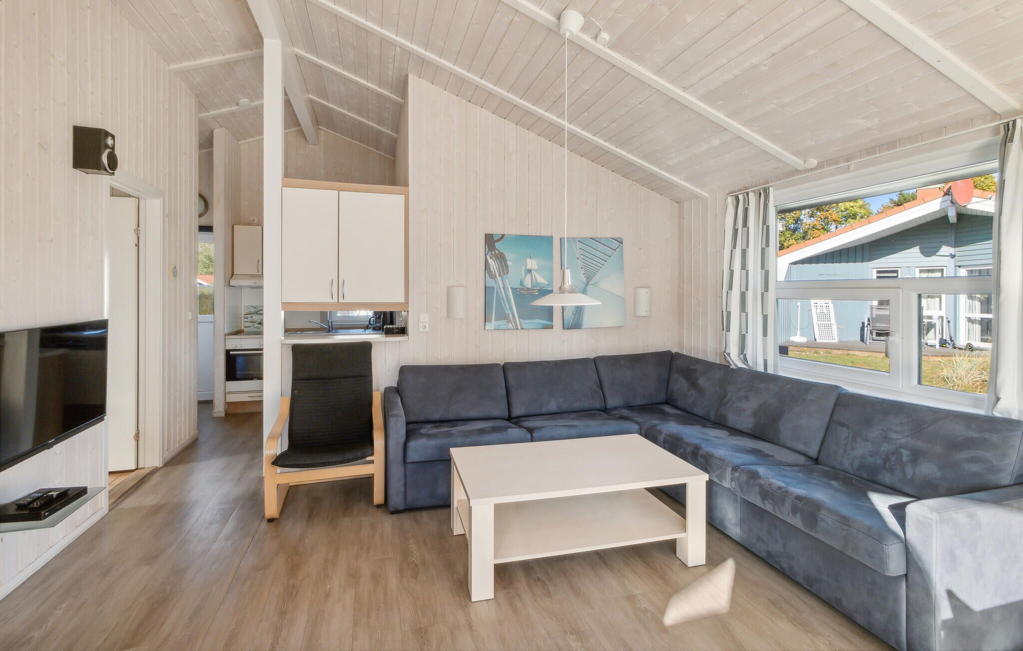 A modern living room with a sectional sofa, a flat-screen TV, and a dining area with a kitchen in the background.
