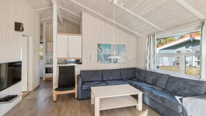 Una sala de estar moderna con un sofá seccional, un televisor de pantalla plana y un comedor con una cocina al fondo.