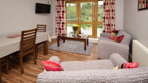 A living room with a wooden dining table, two wooden chairs, a grey sofa, and a coffee table with a vase of flowers. - Apartment 710 Letterfrack  - sleeps 4 guests  in 3 bedrooms (Renvyle)
