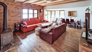 Una sala de estar acogedora con chimenea de ladrillo, un sofá rojo, un sofá marrón y un comedor con mesa y sillas.