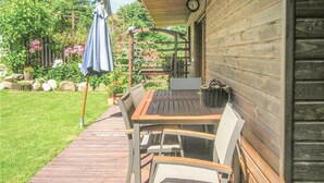 Un patio al aire libre con mesa y sillas de madera, una zona de estar cubierta y un jardín con flores y plantas.