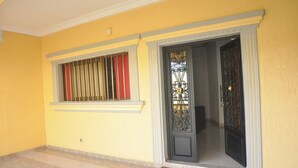 A yellow exterior wall with a window featuring vertical blinds and a decorative door with intricate metalwork.