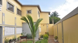 A yellow building with a small garden area, a palm tree, and potted plants.