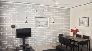 A living room with a flat-screen TV, a ceiling fan, and a dining area with a table and chairs.
