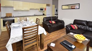 A modern living room with a dining area, a kitchen in the background, and a black leather sofa. - Apartment 702 Letterfrack - sleeps 4 guests  in 3 bedrooms (Unknown)
