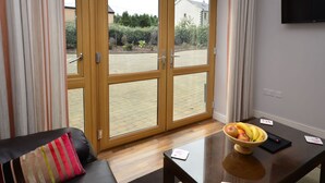 A modern living room with a sofa, a glass coffee table with a fruit bowl, and a sliding glass door leading to an outdoor area. - Apartment 702 Letterfrack - sleeps 4 guests  in 3 bedrooms (Unknown)