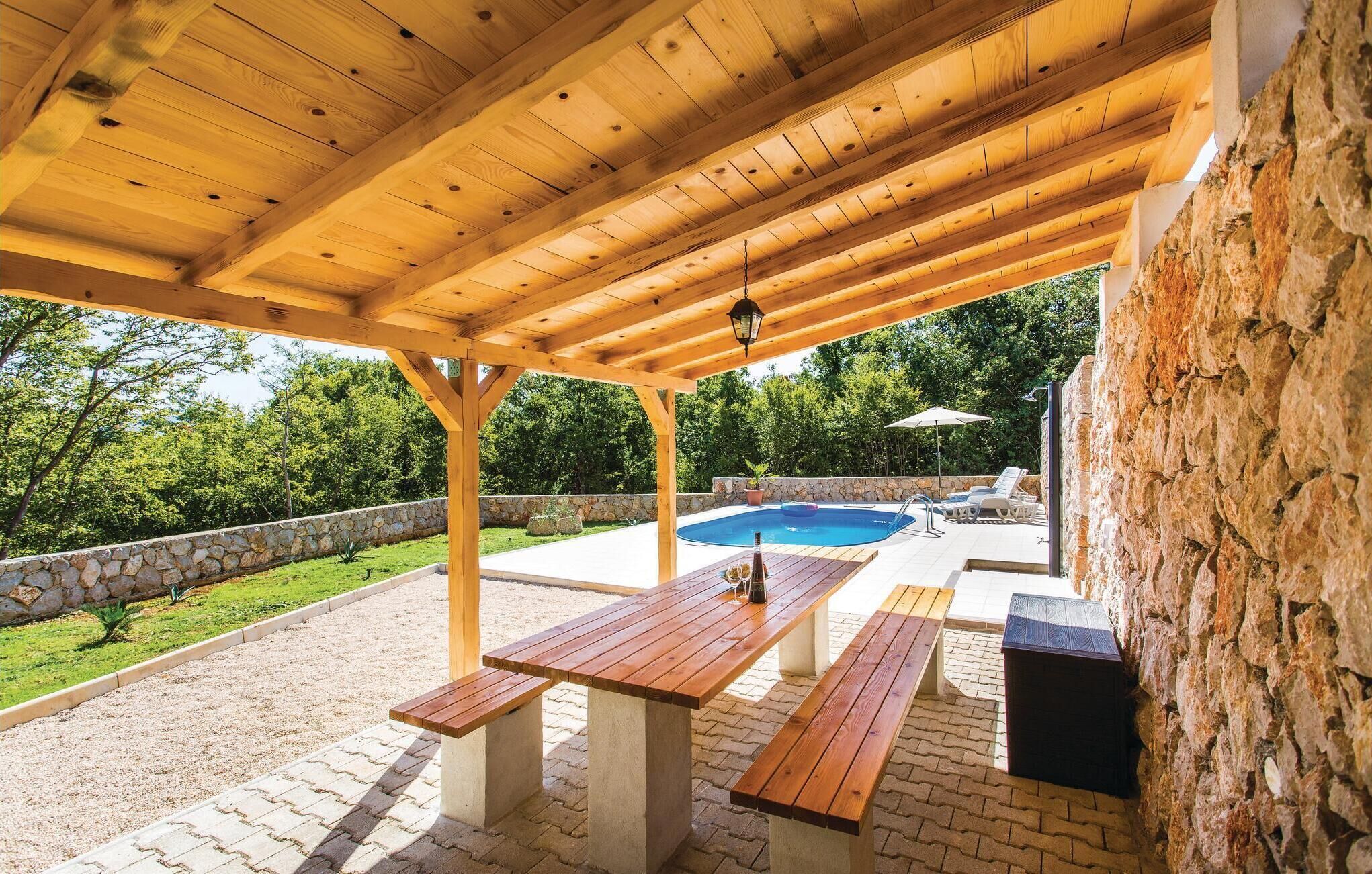 Une terrasse extérieure avec des tables et des bancs en bois, un mur en pierre et une piscine en arrière-plan.