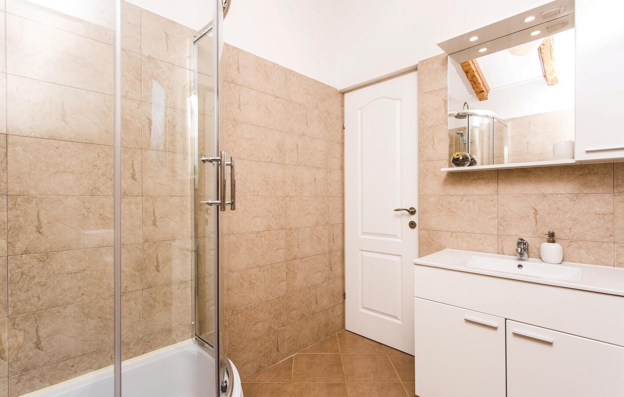A modern bathroom with a glass shower enclosure, a white sink, and a mirror above the vanity.