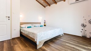 Een slaapkamer met een houten vloer, een bed met bloemenprint beddengoed, een houten plafond en een airconditioning.